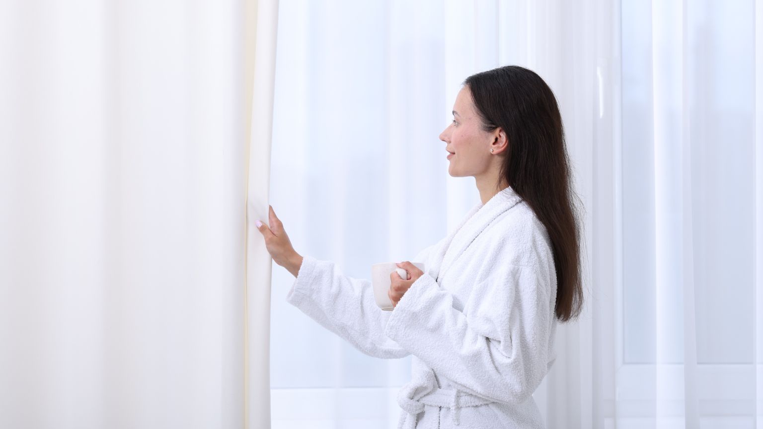 Huésped disfrutando de una vivienda vacacional limpia y luminosa al abrir las cortinas