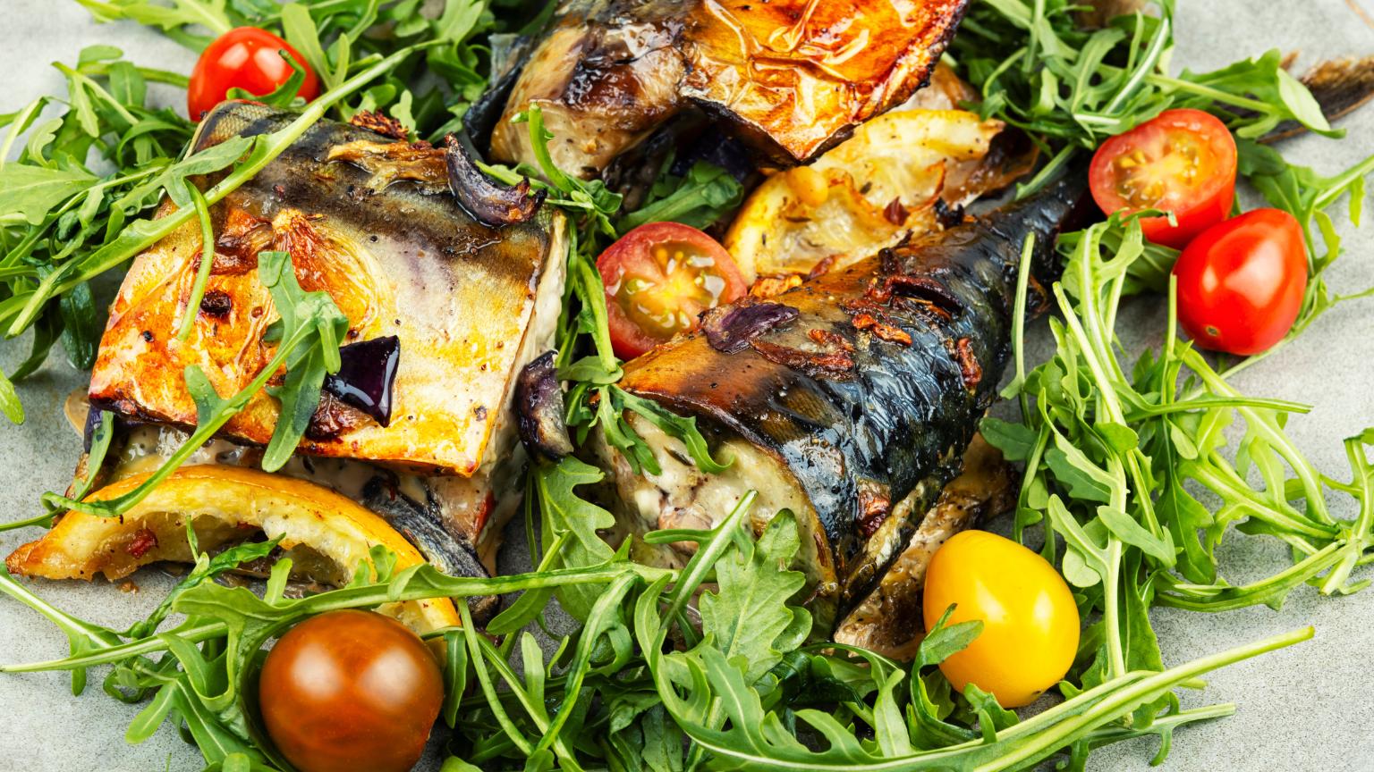 Restaurante mediterráneo con pescado a la brasa, rúcula y tomates frescos en plato tradicional mediterráneo